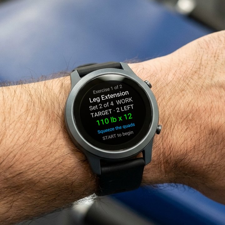 A forearm held out in front of a padded leg extension machine between sets. The slate-grey watch shows BulkForged's next set: Leg Extension, set 2 of 4, 110 lb for 12 reps.